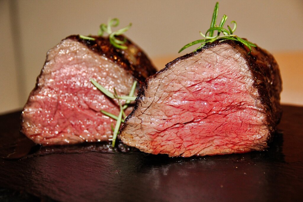 Zwei aufgeschnittene, medium gebratene Rindersteaks mit frischem Rosmarin auf schwarzem Untergrund.