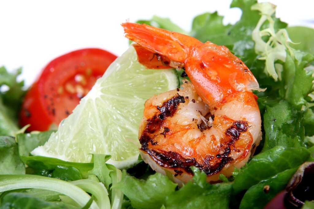 Gegrillte Garnele auf grünem Salat mit Limettenscheibe und einer halbierten Cherrytomate.