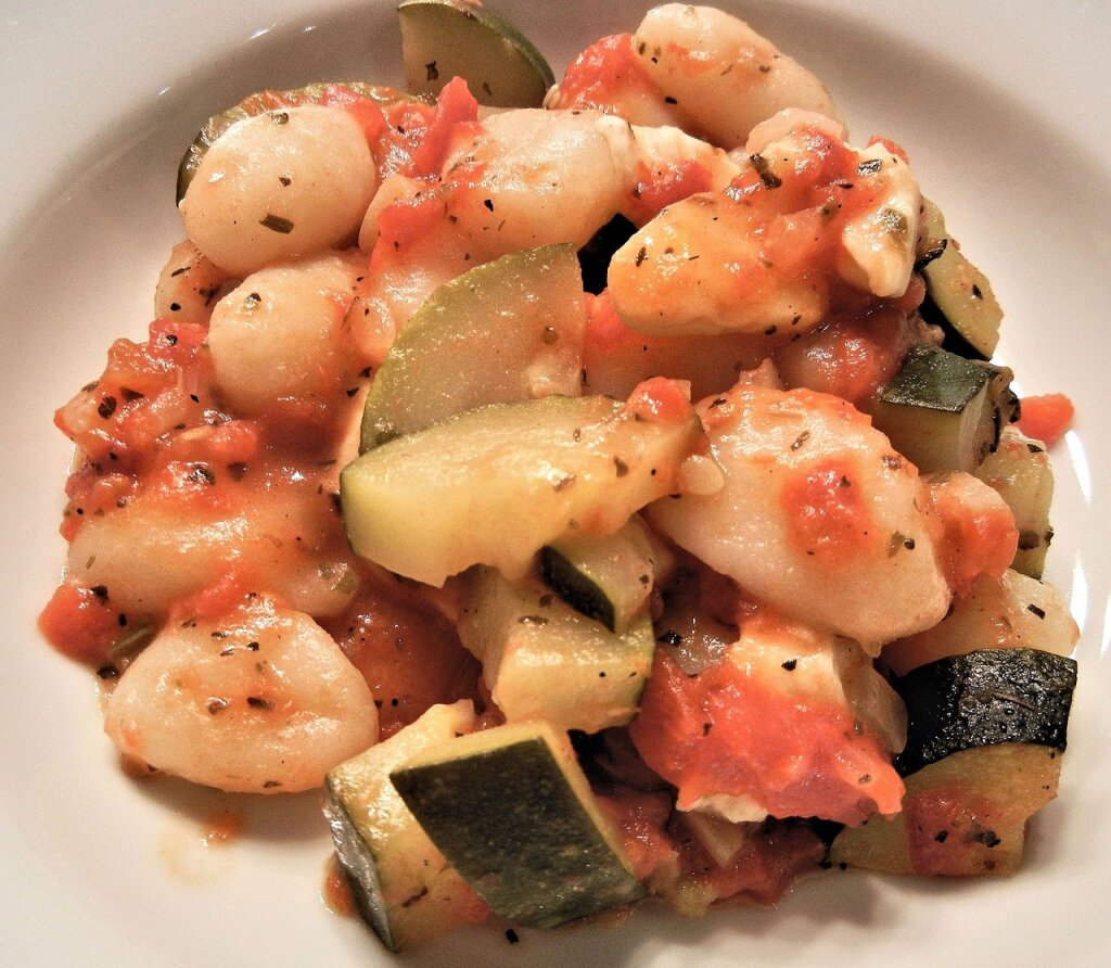 Ein Teller mit Gnocchi, Zucchini und Tomatensoße.