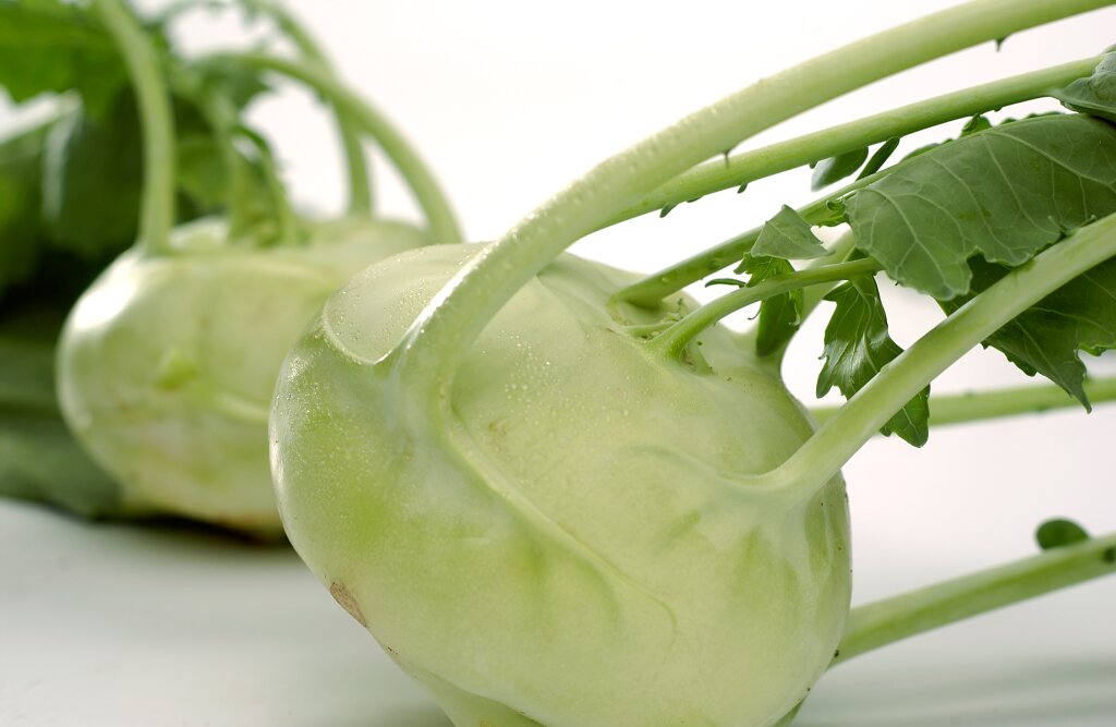 Zwei frische Kohlrabi mit grünen Blättern auf weißem Hintergrund.