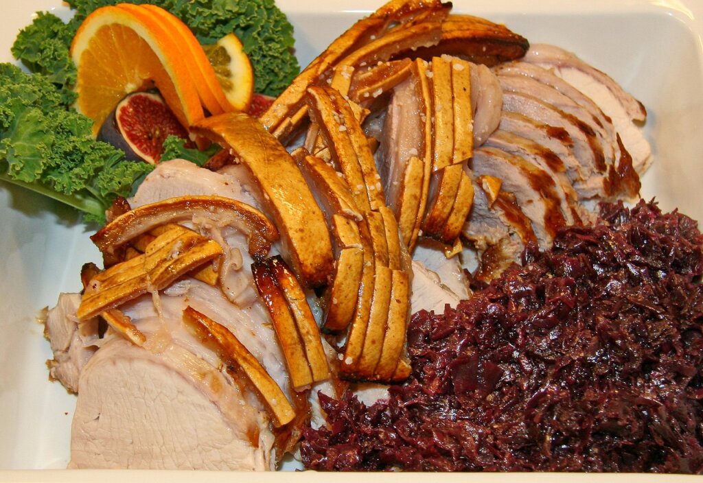 Scheiben von Krustenbraten mit knuspriger Schwarte, Rotkohl und Garnitur aus Grünkohl, Orangenscheiben und Feigen.