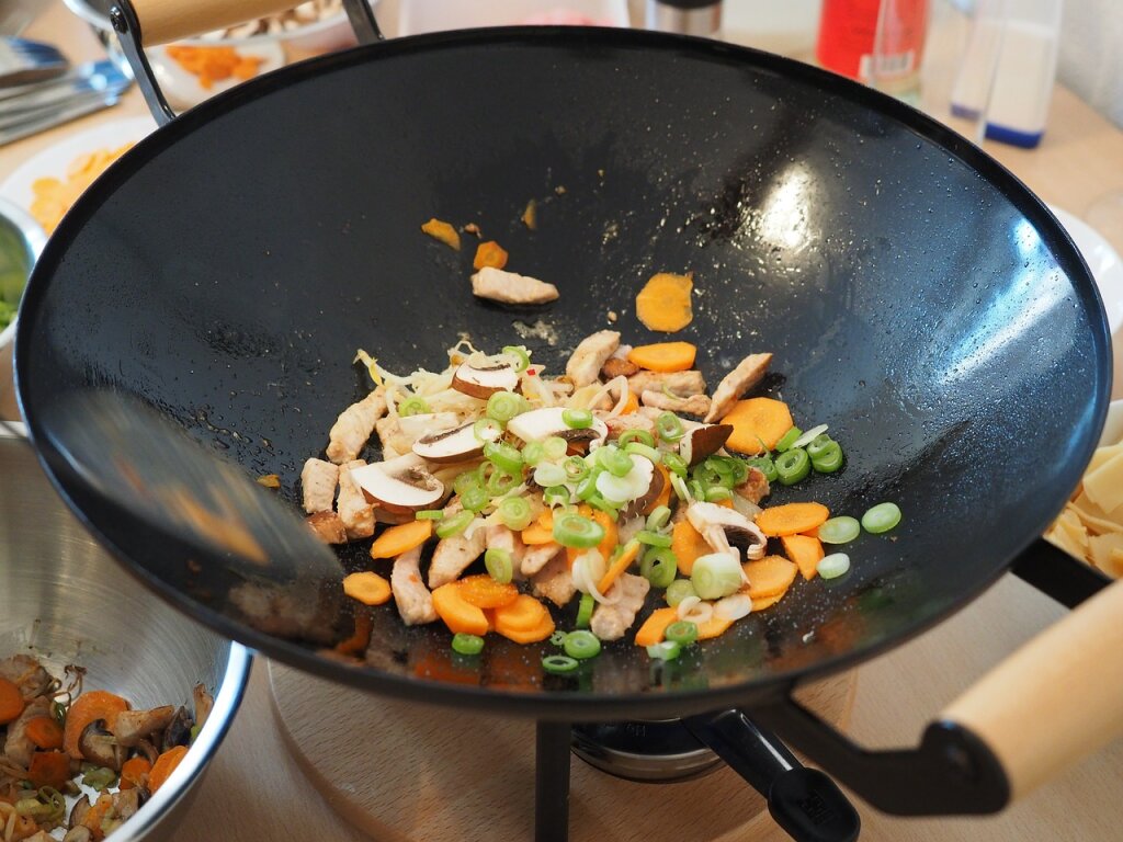Geschnetzeltes Fleisch, Karotten, Lauchzwiebeln und Champignons werden in einem schwarzen Wok angebraten.